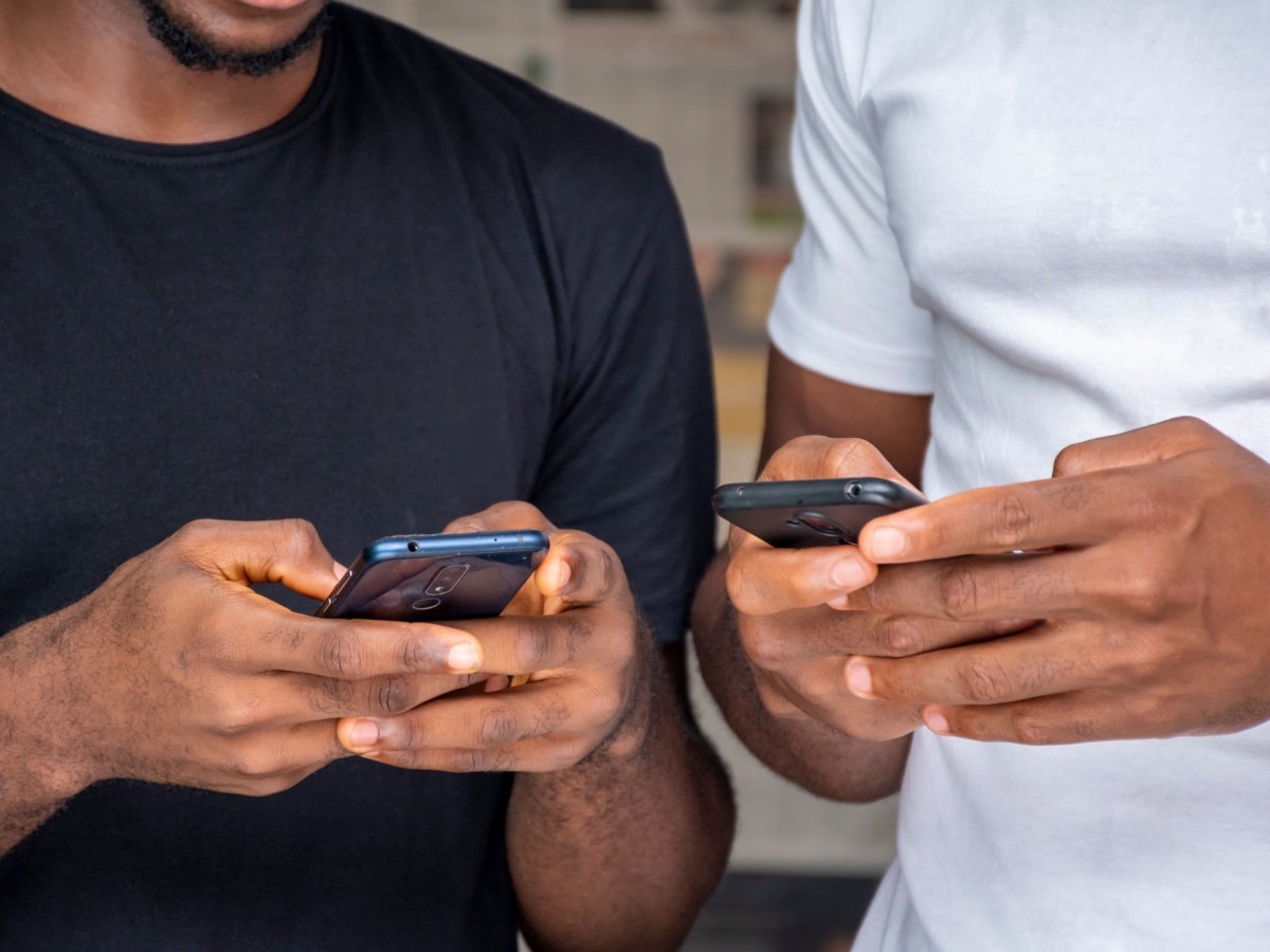 Zwei Menschen stehen nebeneinander und tippen auf den Bildschirmen ihrer Smartphones.