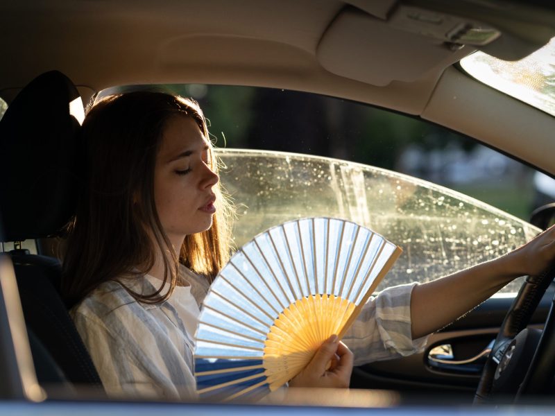 Person sitzt im Auto mit einem Fächer in der Hand.