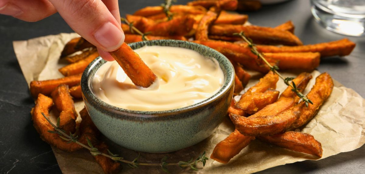 Süßkartoffel-Pommes werden in Mayonnaise getunkt.