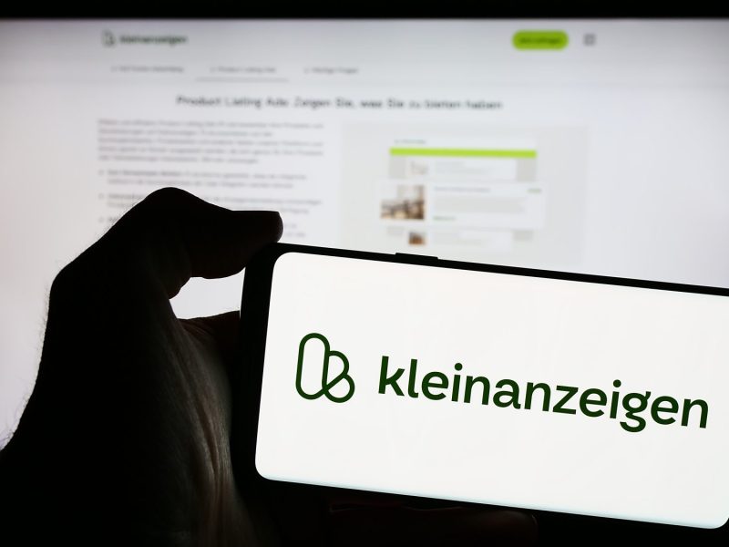 Person hält ein Smartphone in der Hand, auf dem Bildschirm ist das Logo von Kleinanzeigen zu sehen,