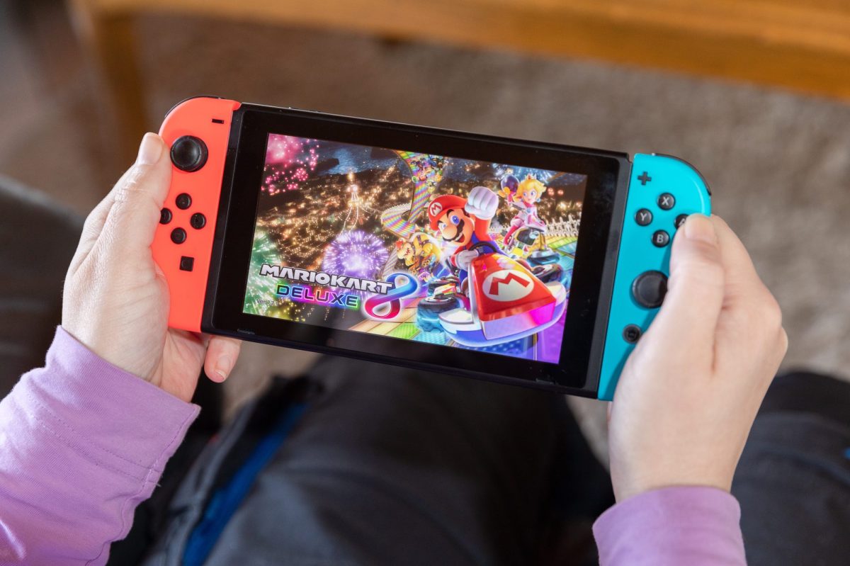 Person hält eine Nintendo Switch in der Hand, auf der Mario Kart läuft.