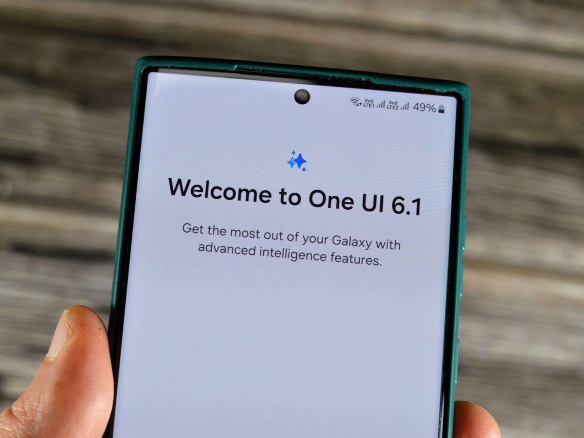 Person hält Smartphone in der Hand. Auf dem Bildschirm steht "Welcome to One UI 6.1".