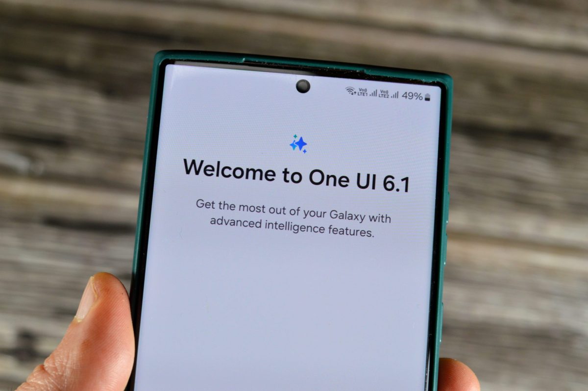 Person hält Smartphone in der Hand. Auf dem Bildschirm steht "Welcome to One UI 6.1".