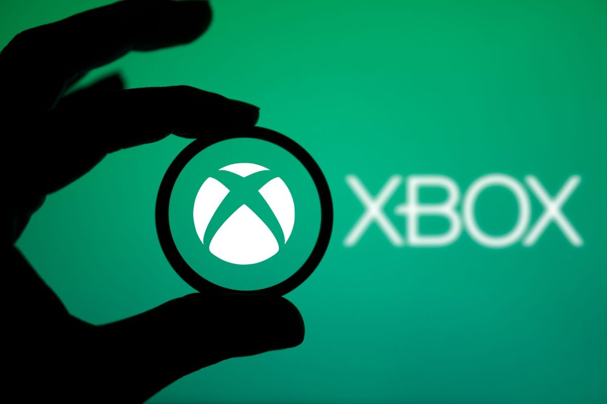 Das Xbox-Logo ist auf einem grünen Hintergrund zu sehen. Im Vordergrund ist der Schatten einer Hand zu sehen.