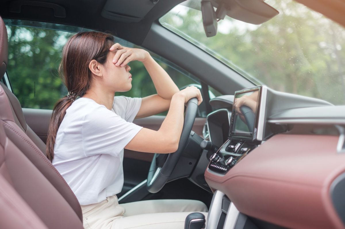 Frau sitzt am Steuer eines Autos und hält sich verzweifelt die Hand vor das Gesicht.