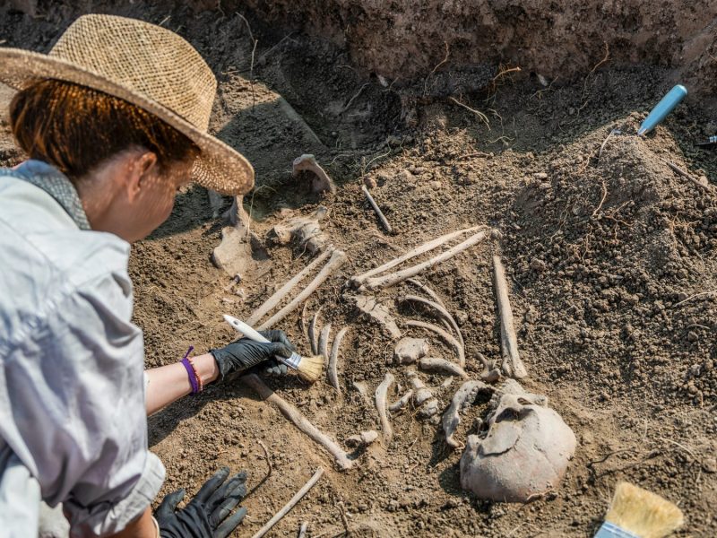 Frau arbeitet mit Werkzeug an einem archäologischen Fund.