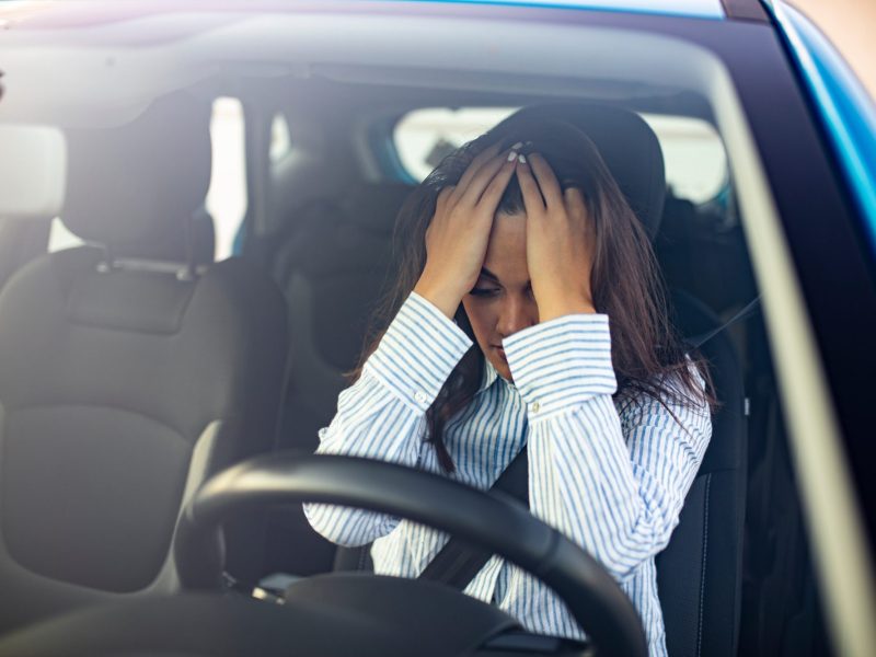 Verzweifelte Person hält sich im Auto die Hände vors Gesicht.