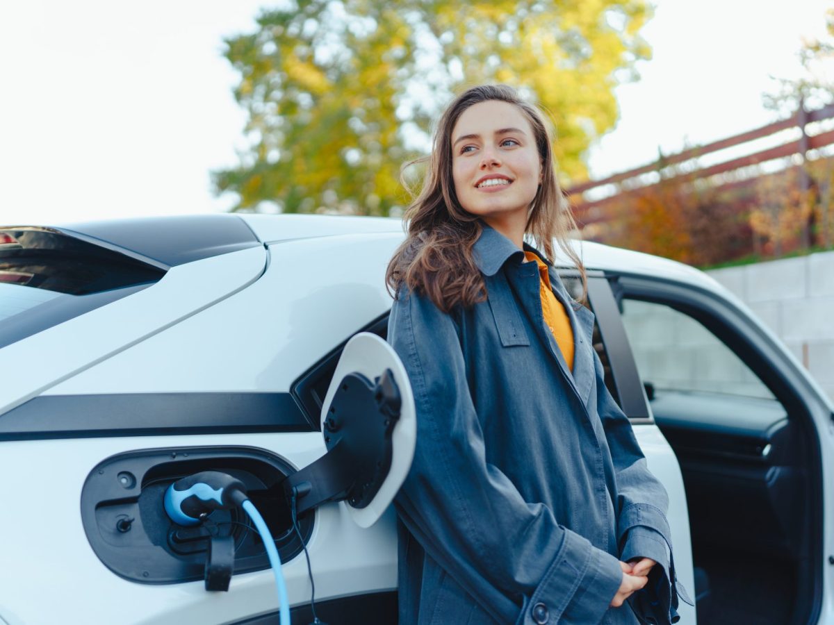 Frau lehnt an einem Elektroauto, das gerade geladen wird.