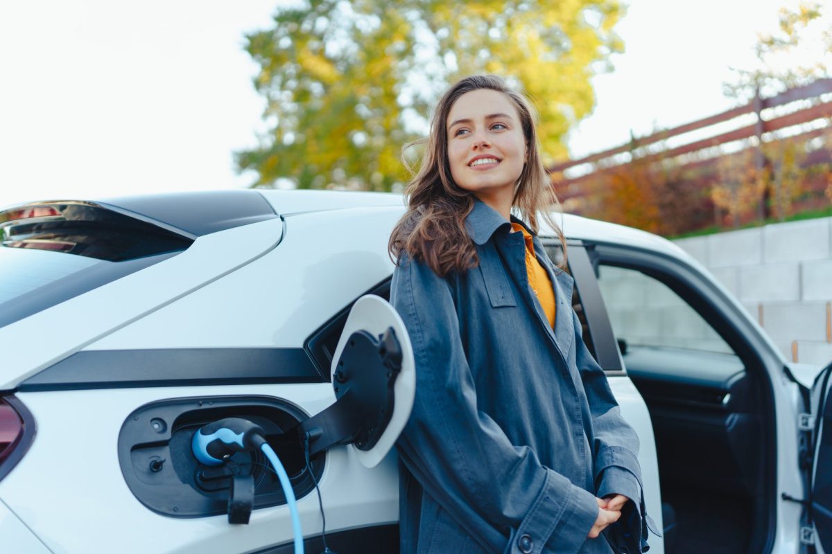 Frau lehnt an einem Elektroauto, das gerade geladen wird.