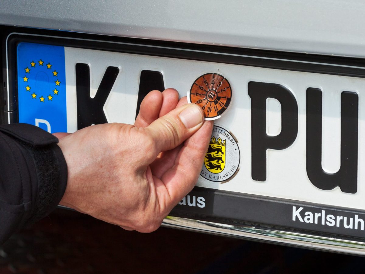 Person drückt oder löst die TÜV-Plakette am Auto.