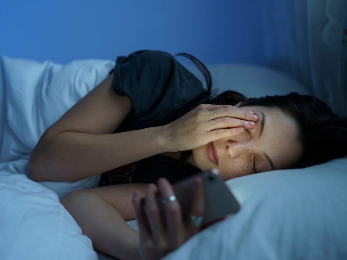 Person liegt im Bett und hält ein Handy in der Hand.