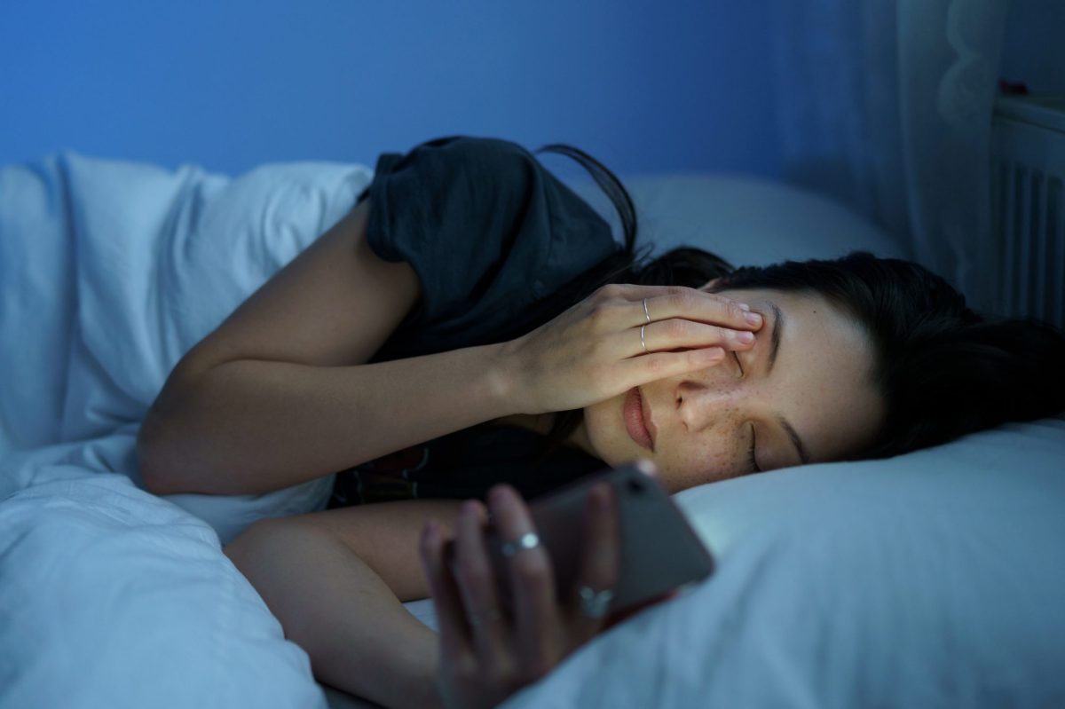 Person liegt im Bett und hält ein Handy in der Hand.