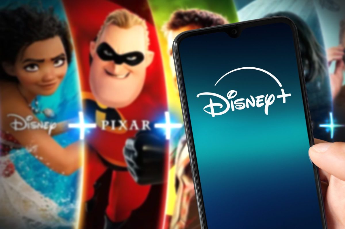 Auf einem Handy-Display wird das Disney+-Logo angezeigt. Im Hintergrund sind Charaktere aus Animationsfilmen zu sehen.