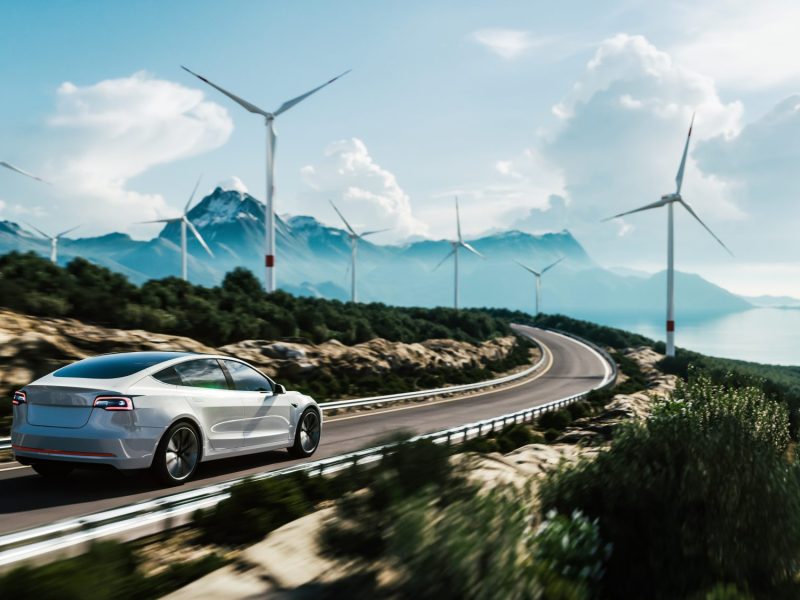 Elektroauto auf einer Autobahn mit Windrädern im Hintergrund.