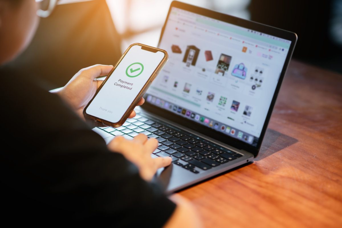 Person sitzt vorm Laptop und bezahlt Online via Handy.
