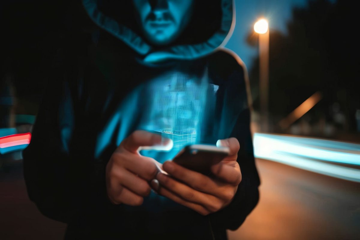 Person mit Kapuze überm Kopf hält ein Handy in der Hand.