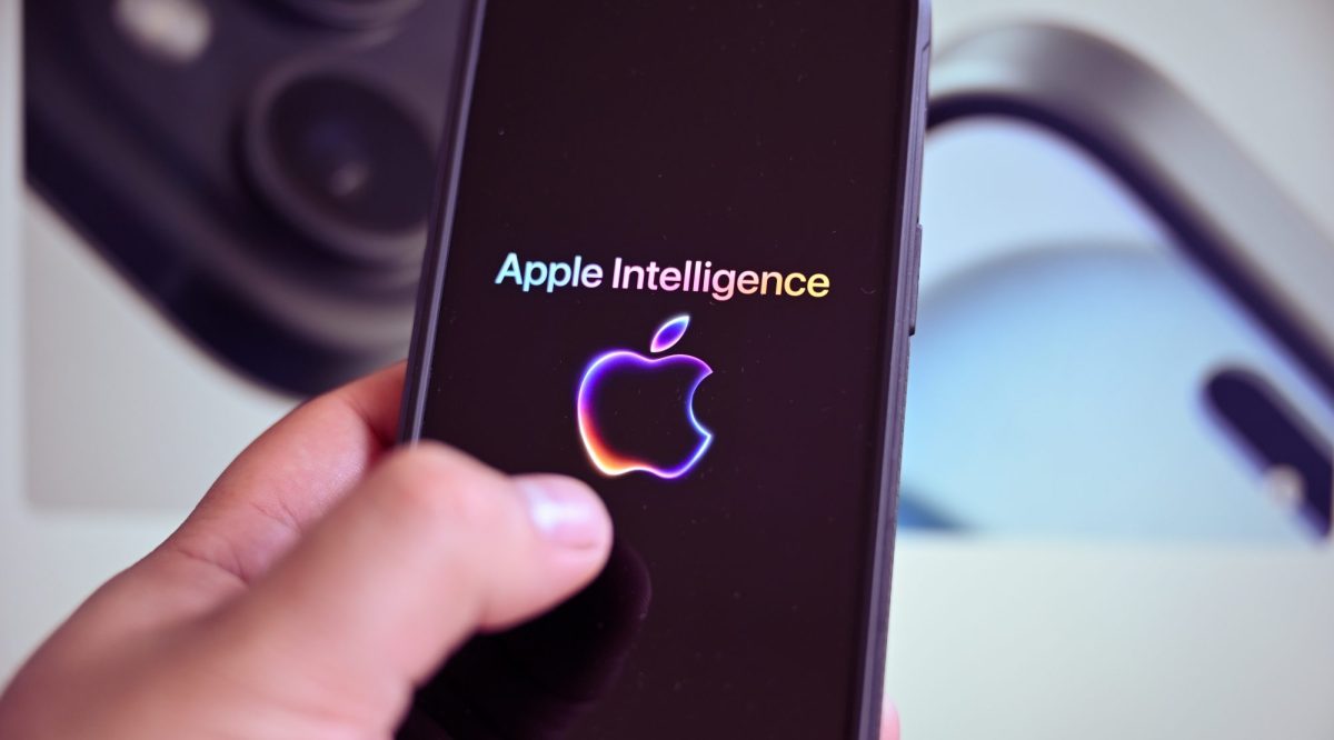 Eine Person hält ein Handy in der Hand. Auf dem Display wird das Logo von Apple Intelligence angezeigt.