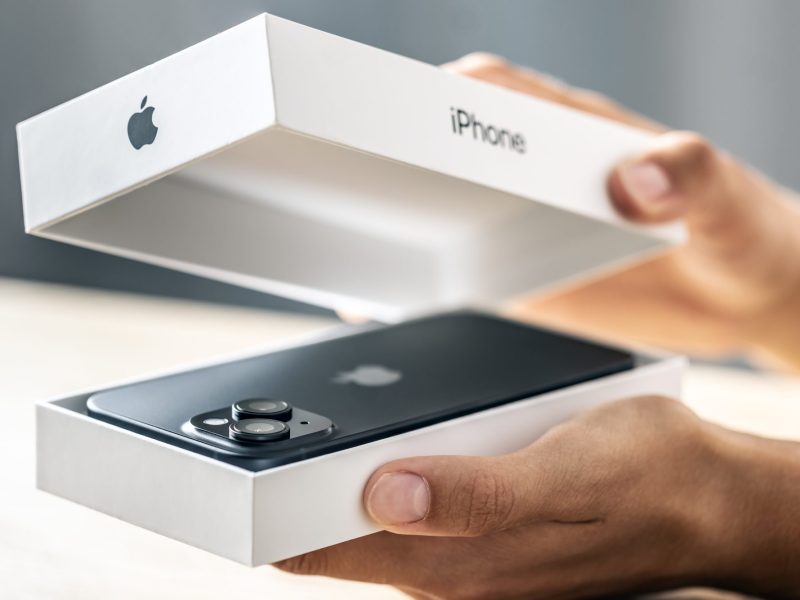 Eine Person öffnet eine Verpackung, in der sich ein iPhone befindet.