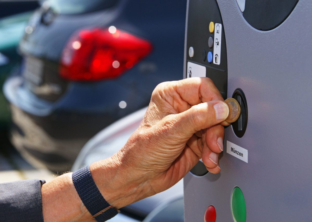 Eine Person wirft eine Münze in eine Parkscheinautomaten.