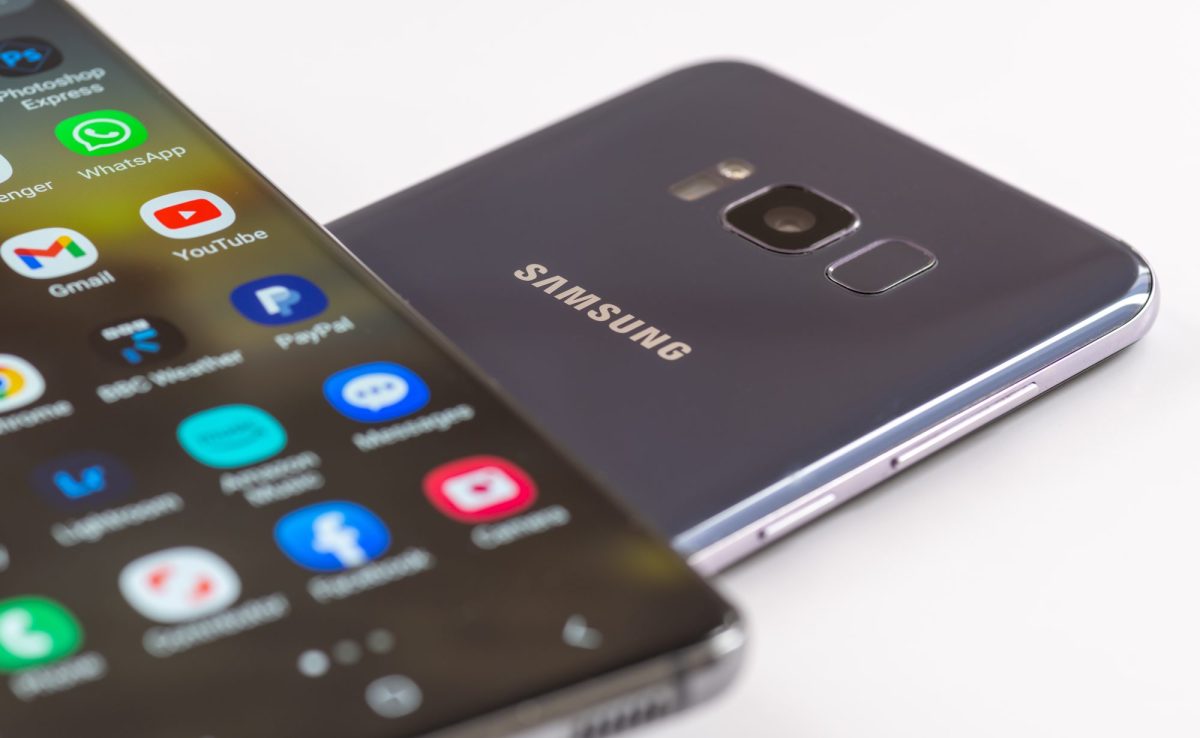 Auf einem Handy-Display werden verschiedene Apps angezeigt. Darunter liegt ein Handy, auf dessen Rückseite das Samsung-Logo abgebildet ist.
