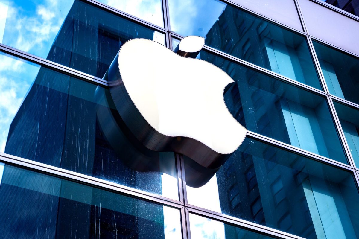 Apple-Logo an einer Glasfassade, die das Blau des Himmels reflektiert.