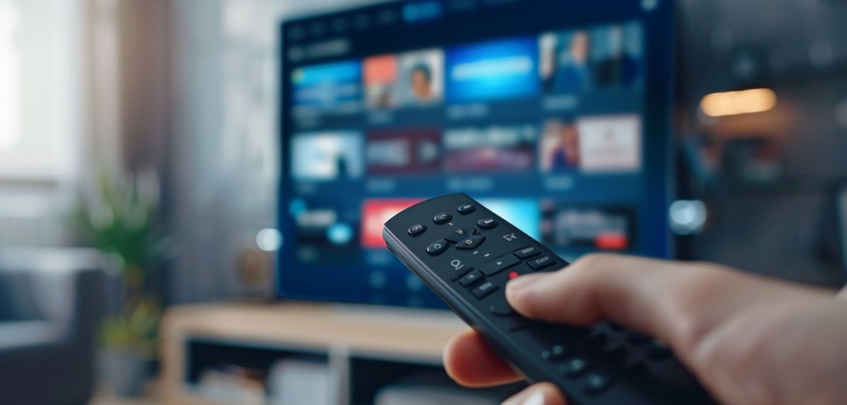 Person hält eine Fernbedienung auf einen Fernseher.