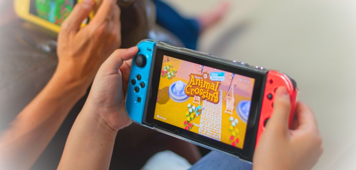 Person hält eine Nintendo Switch in der Hand. Auf der Konsole wird Animal Crossing angezeigt.
