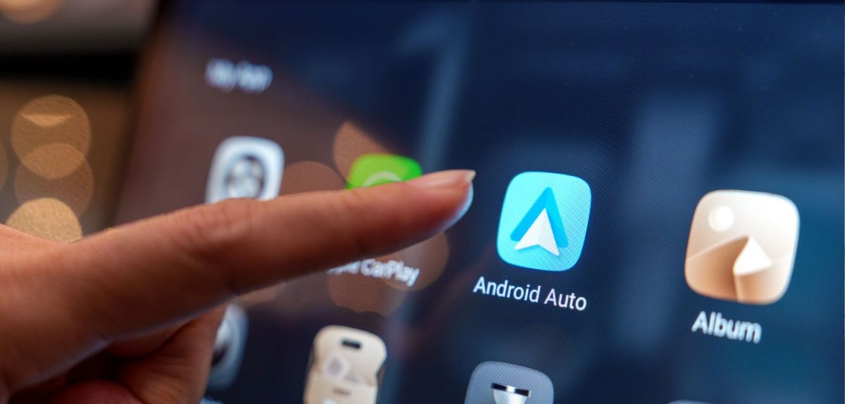 Person zeigt mit einem Finger auf Android Auto-App auf einem Display.