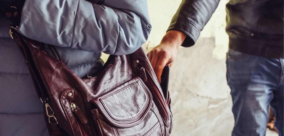 Person klaut ein Handy aus einer Tasche.