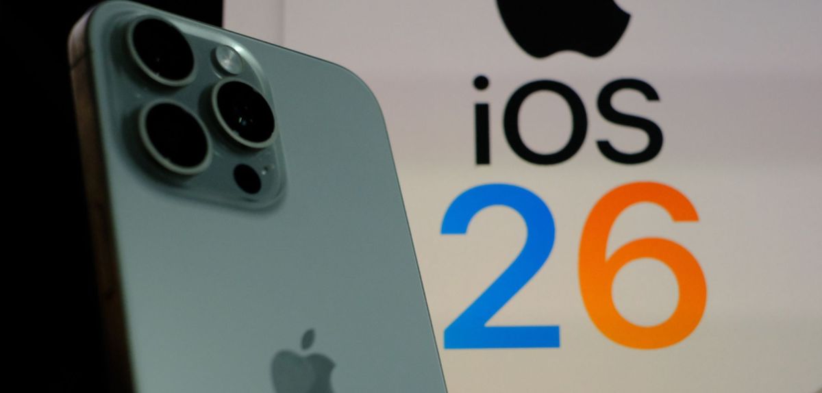 Ein iPhone und im Hintergrund steht iOS 26.