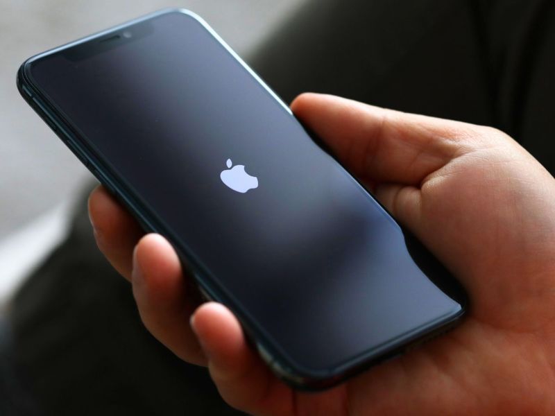 Person hält ein iPhone in der Hand. Auf dem Display ist das Apple-Logo zu sehen.