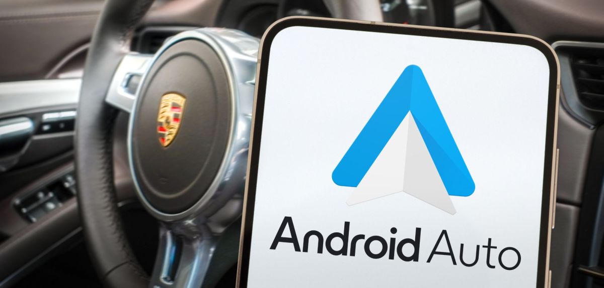 Android Auto wird auf einem Handy angezeigt. Im Hintergrund ist der Innenraum eines Autos zu sehen.
