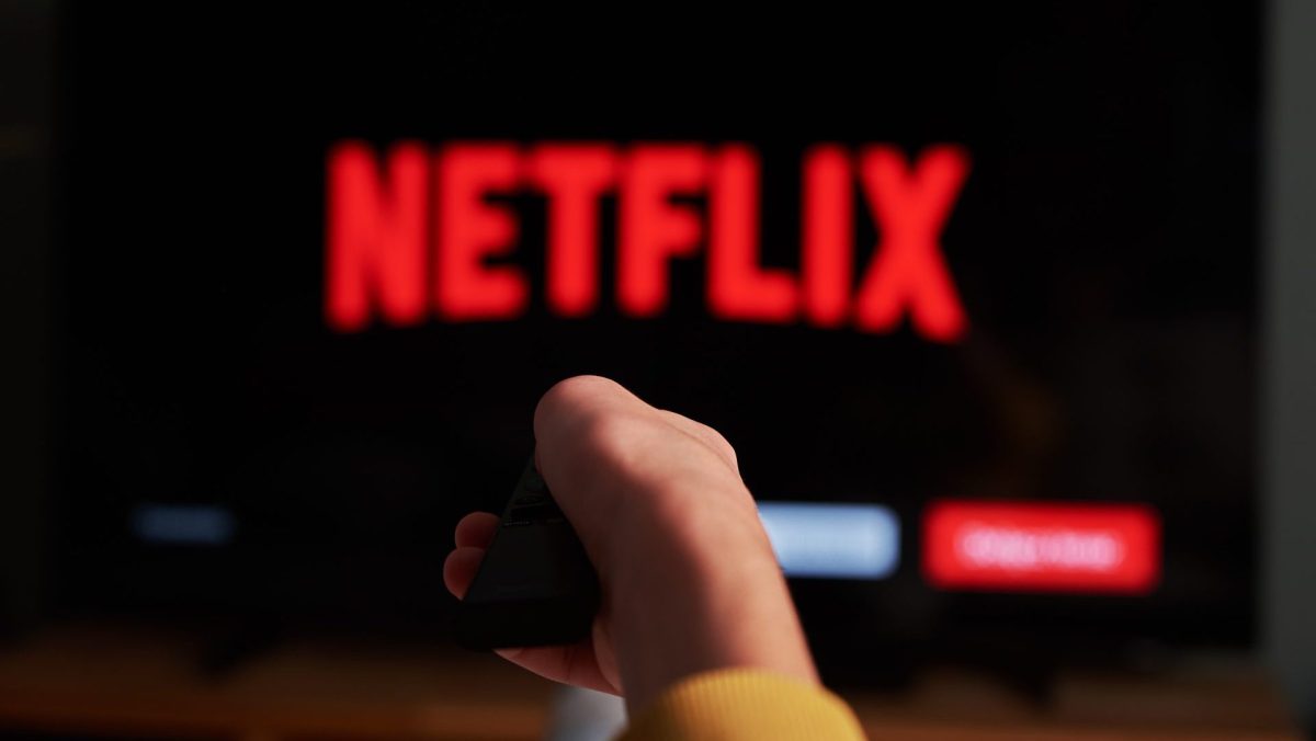 Person hält die Fernbedienung in Richtung Fernseher mit Netflix-Logo