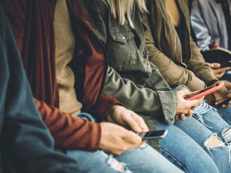 Personen sitzen jeweils mit einem Smartphone in der Hand nebeneinander.
