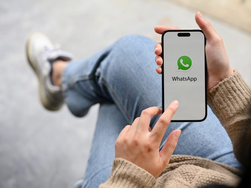 Person, die sitzt und währenddessen WhatsApp auf dem Handy öffnet.