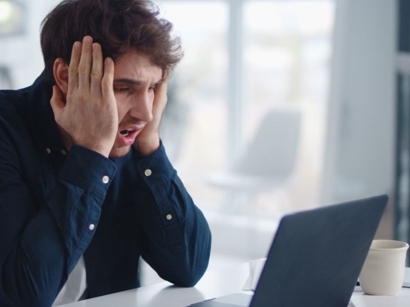 Person sitzt vor einem Laptop und schlägt die Hände vor dem Gesicht zusammen.